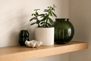 Decorative shelf styling with indoor plants, ceramic accessories and green glass vases on an oak floating shelf.